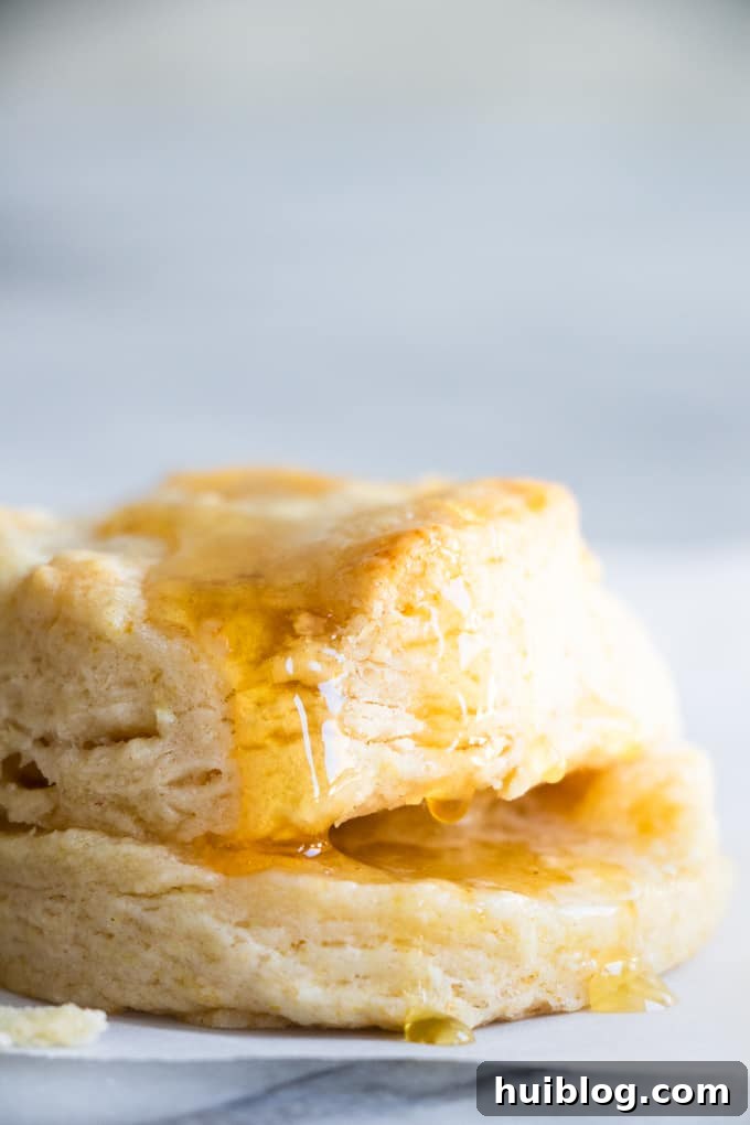 Fluffy Southern Biscuits from Scratch 14 A glorious homemade biscuit split in half, generously spread with butter, and stacked with another biscuit, both adorned with drizzles of honey, highlighting its perfect flakiness and delicious appeal.