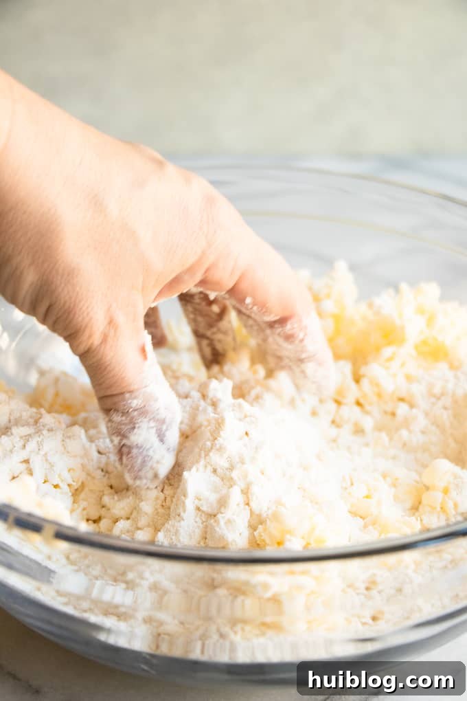 Fluffy Southern Biscuits from Scratch 5 A hand gently mixing cold grated butter into the flour mixture, illustrating the careful touch required to create tender homemade biscuits.