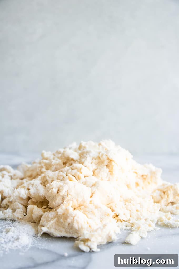 Fluffy Southern Biscuits from Scratch 6 A mound of crumbly biscuit dough, just combined, resting on a marble surface, awaiting the gentle pressing and folding process for perfect homemade biscuits.