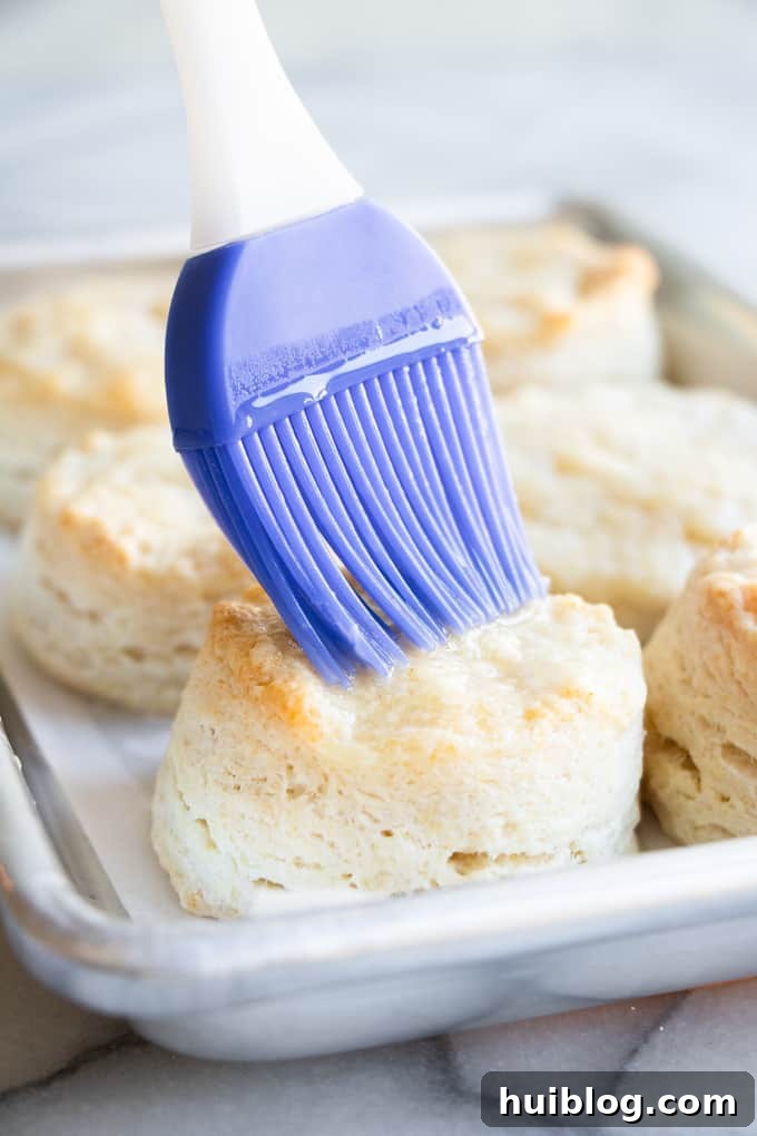 Fluffy Southern Biscuits from Scratch 9 Freshly baked homemade biscuits receiving a generous brushing of melted butter, enhancing their golden crust and rich flavor.