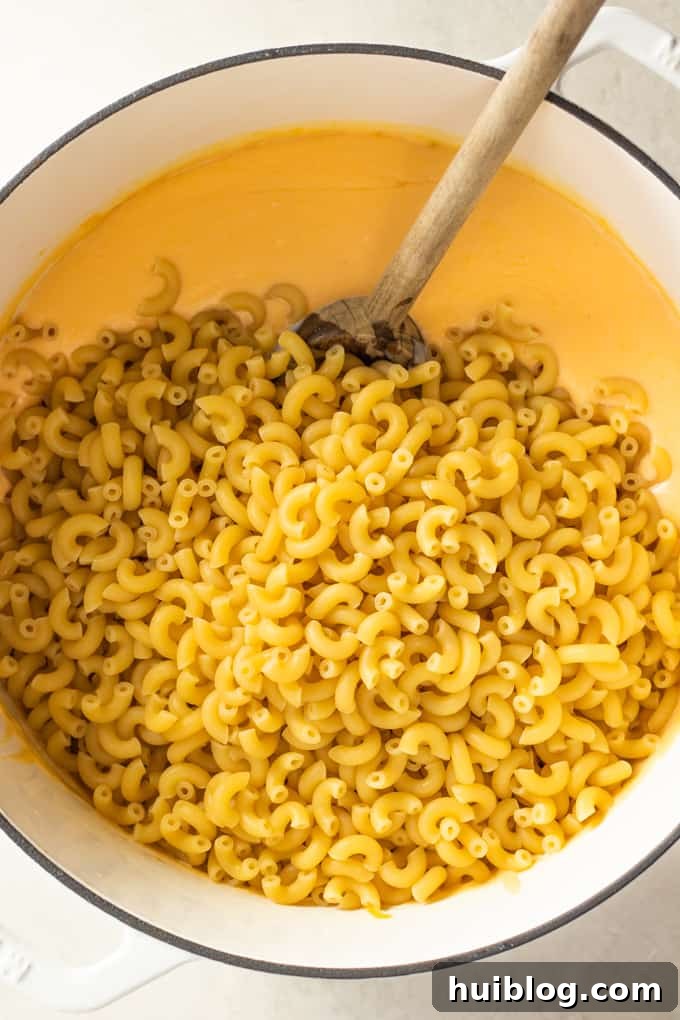 Golden Baked Mac and Cheese Made Easy 5 Elbow macaroni noodles added to a large dutch oven of homemade cheese sauce for macaroni and cheese.