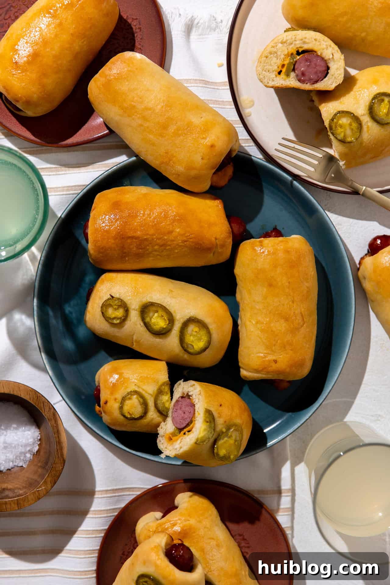 Texas Klobasnek Sausage Kolaches 2 Freshly baked Texas style kolaches on a plate, some topped with jalapeños and cut open to show the melted cheese and jalapeño inside.