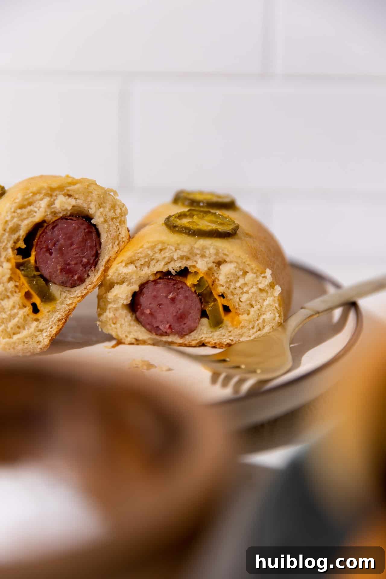 Texas Klobasnek Sausage Kolaches 10 A Texas Sausage Kolache cut open, revealing the savory filling of sausage, melted cheese, and sliced jalapeños inside the fluffy bread.
