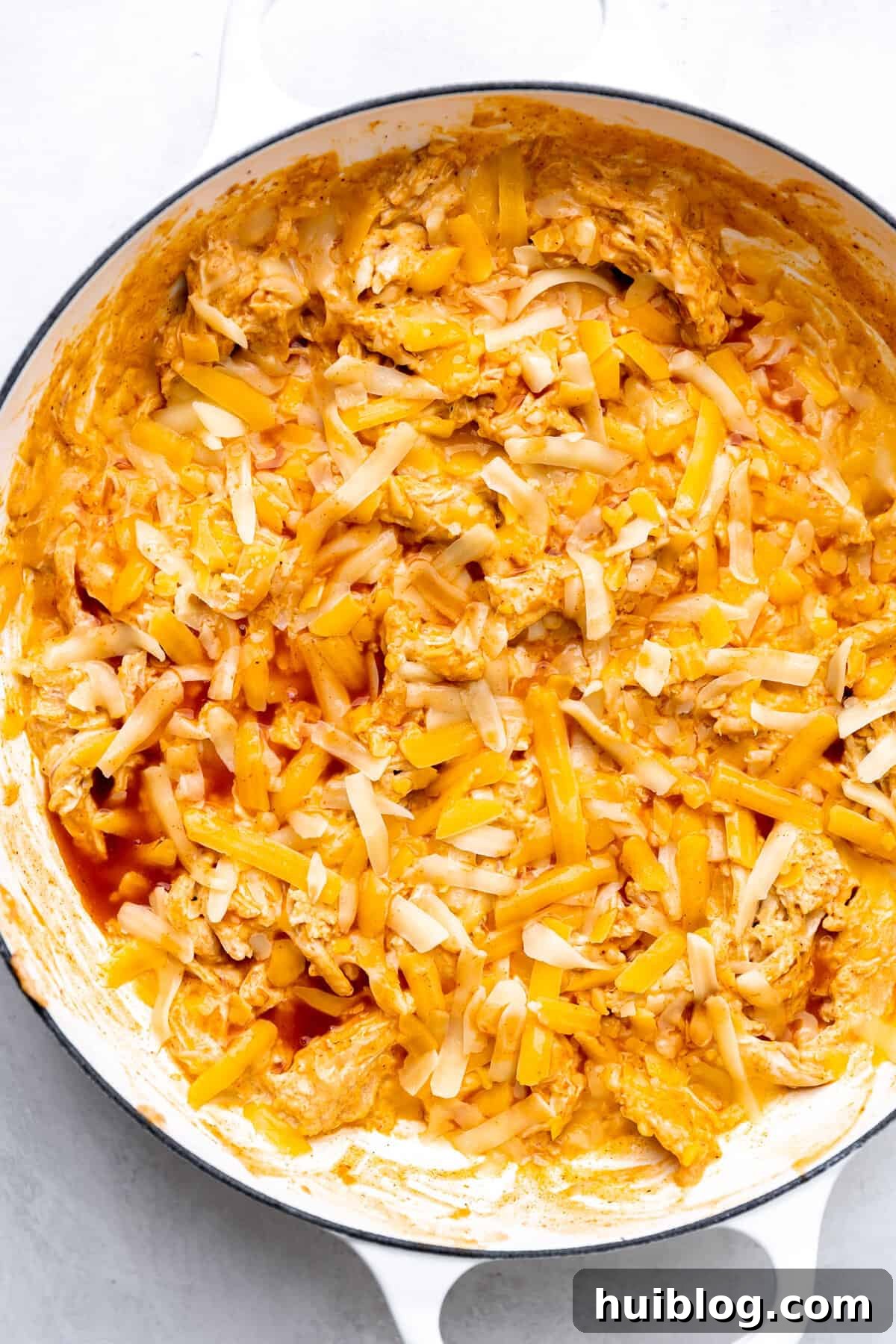 Loaded Cheesy Chicken Enchilada Dip 5 White skillet with chicken enchilada dip ready to bake.