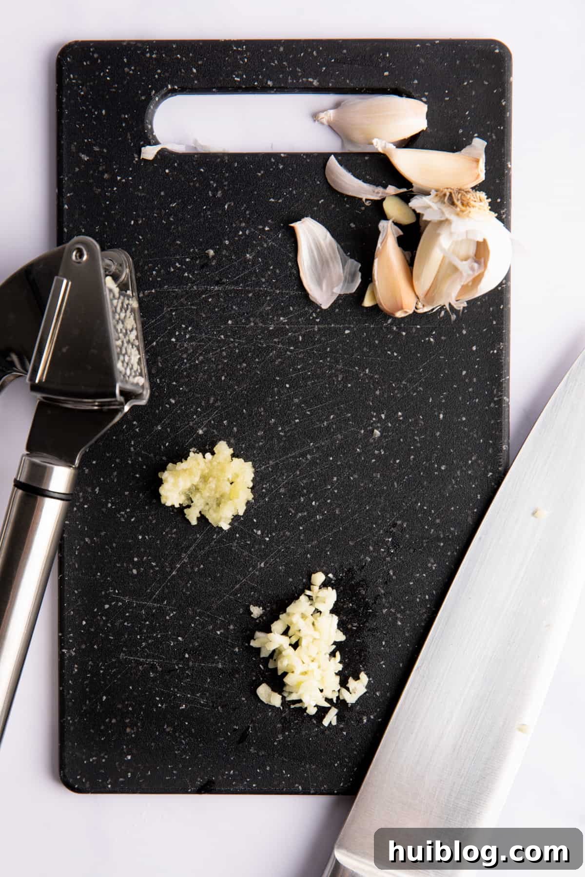 Garlic minced with a knife and with a garlic press on a black cutting board.