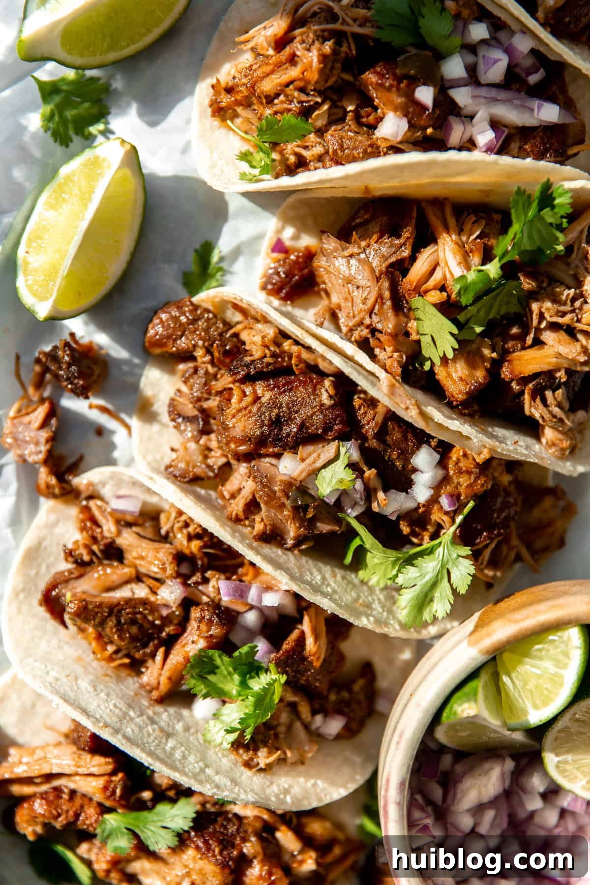 Delicious carnitas tacos garnished with diced onions and fresh cilantro, perfectly lined up and ready to be enjoyed.