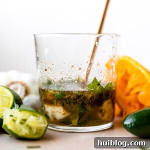 Glass filled with carnitas marinade, lime wedges, orange wedges surrounded and a gold spoon in the cup.