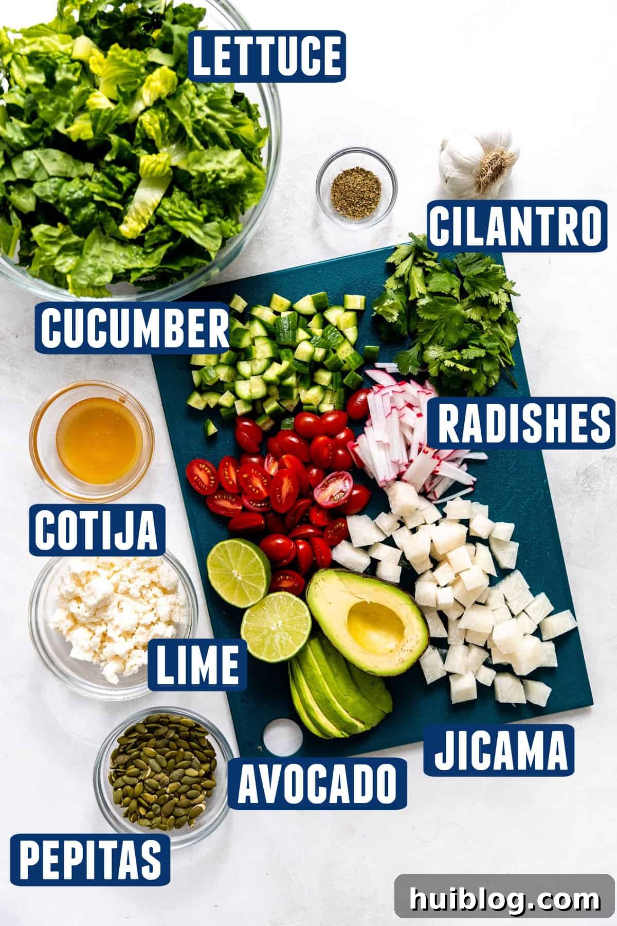 Fiesta Salad Bowl 3 Ingredients needed to make a mexican salad laid out on the counter, with various fresh vegetables including romaine, radishes, jicama, and avocado on a cutting board.