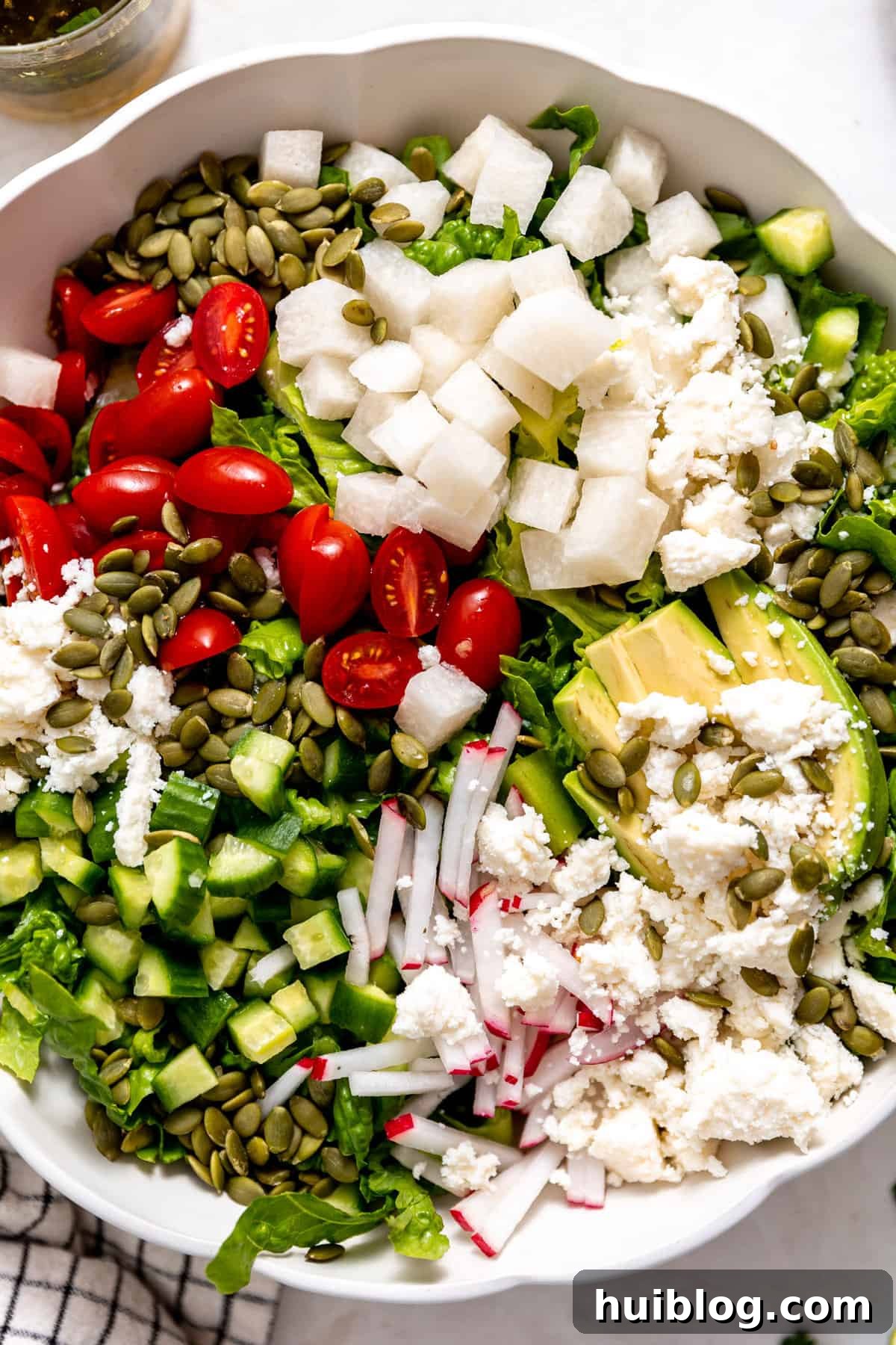Fiesta Salad Bowl 5 Up close view of a white bowl with layers of salad ingredients over romaine lettuce, showing radish, jicama, and avocado.
