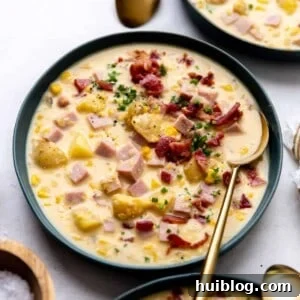 Bowl of hearty corn chowder, garnished with crispy bacon bits and fresh green chives.