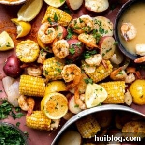 A sumptuous shrimp boil, spread generously on butcher paper, accompanied by a shaker of Old Bay seasoning, bottles of beer, and a luscious garlic butter sauce.