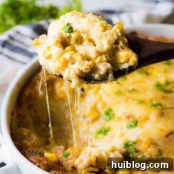 A spoon scooping out a generous portion of cheesy corn casserole, with enticing strings of melted cheese stretching away.