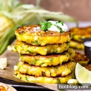 Stack of cheesy corn fritters topped with sour cream and cilantro.