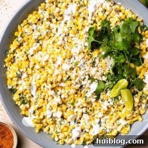 Serving bowl filled with creamy elote corn salad, garnished with cilantro and chili powder.