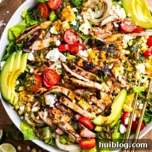 White bowl of grilled chicken salad, featuring grilled chicken pieces, bell peppers, corn, and onion on a bed of fresh greens.
