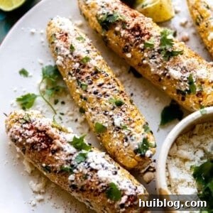 Plate of Mexican street corn (Elotes) with crumbled cotija cheese, lime wedges, and fresh cilantro.