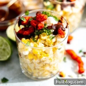 Esquites, or Mexican street corn served in a cup, generously topped with crumbled queso fresco, fiery Hot Cheetos, fresh cilantro, and a drizzle of chile sauce.
