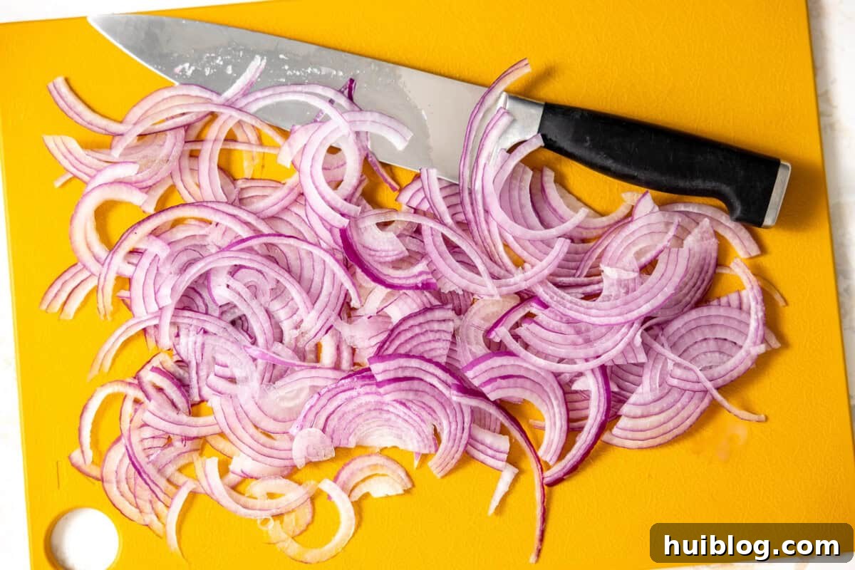 My Secret Weapon Pickled Red Onions 6 Red onion thinly sliced on a cutting board with a black-handled knife.