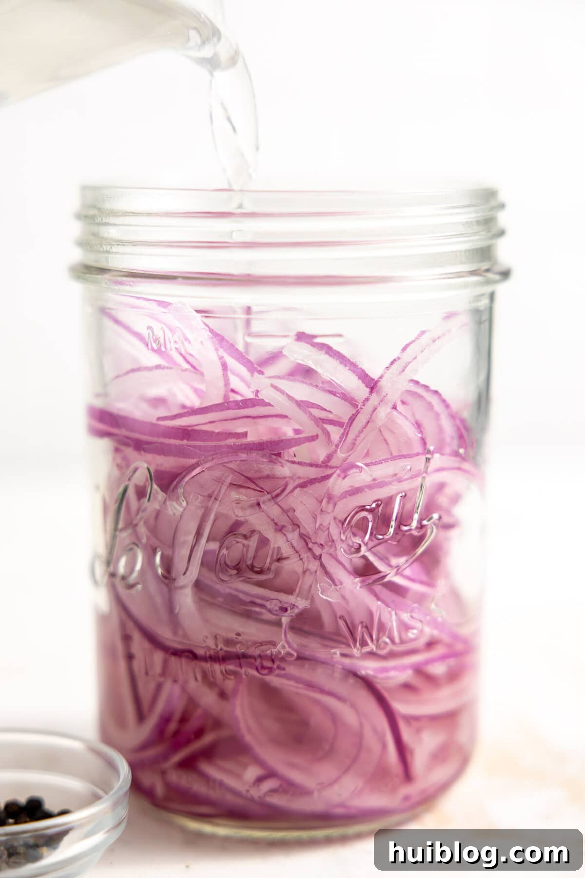 My Secret Weapon Pickled Red Onions 8 Pouring vinegar over thinly sliced red onions in a jar to make easy pickled onions.
