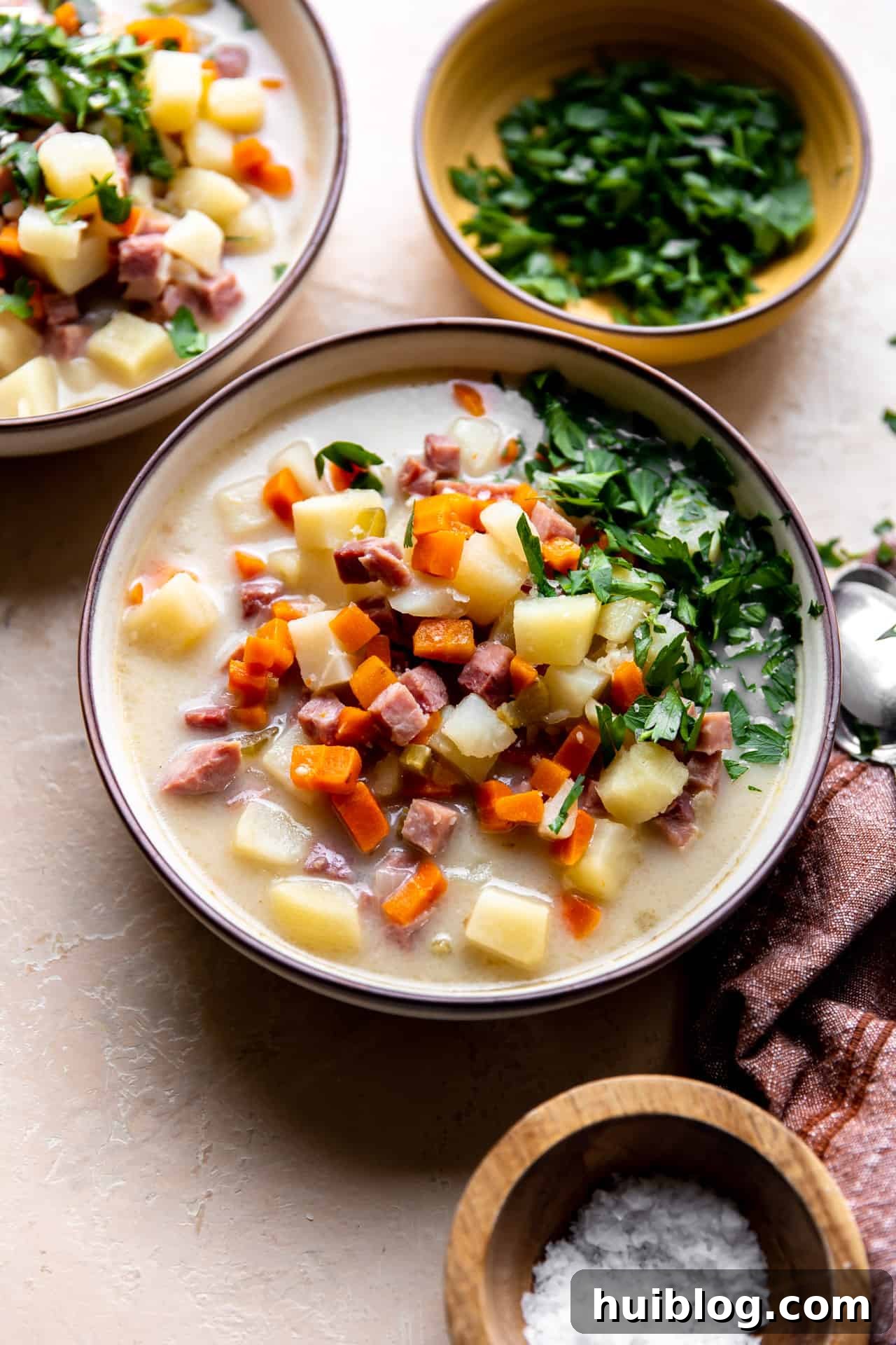 A steaming bowl of homemade ham bone soup, garnished with fresh parsley, highlighting its rich, creamy texture and generous chunks of ham and vegetables.