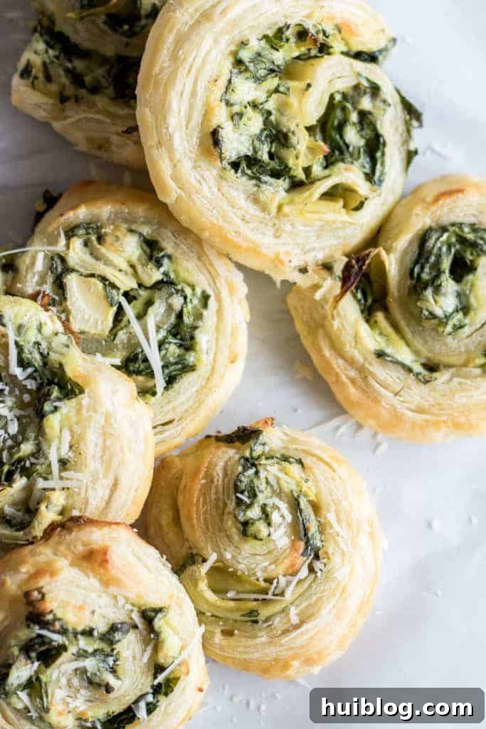 Flaky Spinach Artichoke Swirls 2 Deliciously golden Puff Pastry Spinach and Artichoke Pinwheels on a baking sheet, ready to be served as an appetizer or snack.