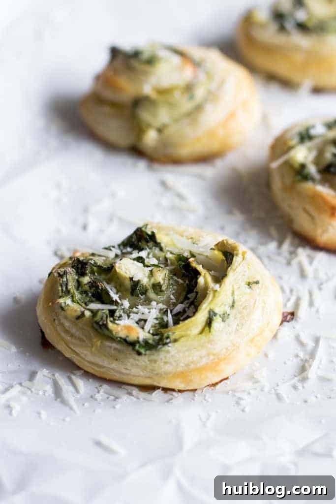 Flaky Spinach Artichoke Swirls 3 Close-up of a freshly baked Puff Pastry Spinach and Artichoke Pinwheel, showcasing its flaky layers and visible filling.
