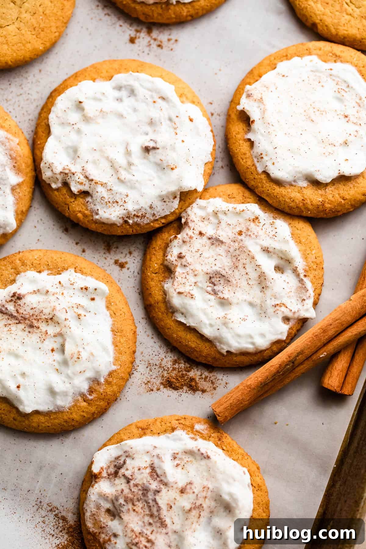 overhead shot of pumpkin cookies topped with cream cheese frosting and arranged on a baking sheet lined with parchment paper.