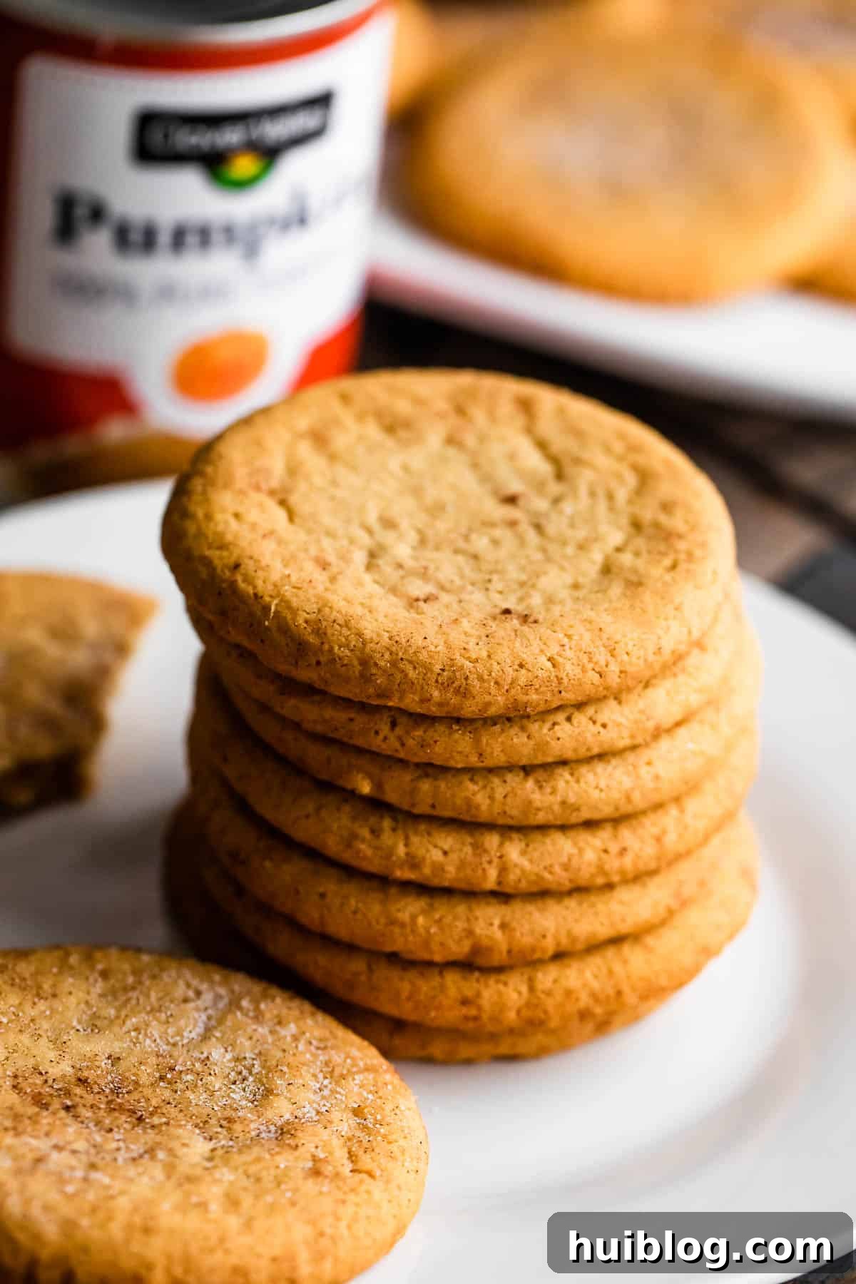 a stack of pumpkin cookies arranged on a white plate with a can of pumpkin set right behind the plate.