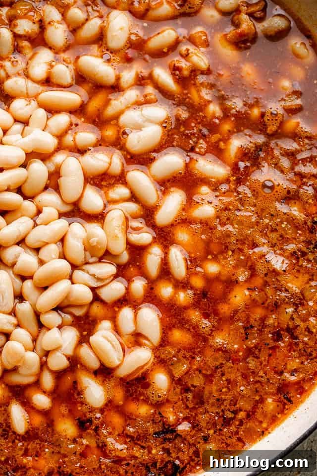 Sweet and Smoky Maple Bacon Baked Beans 5 Beans simmering in a rich, dark sauce in a pot on the stovetop.