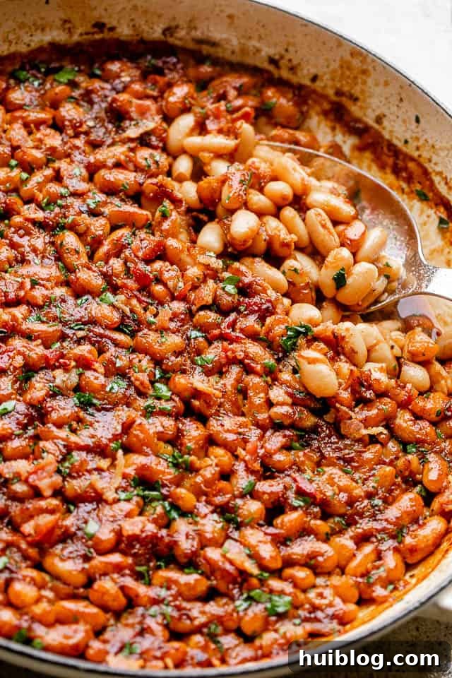 Sweet and Smoky Maple Bacon Baked Beans 6 A serving spoon scooping out a generous portion of maple bacon baked beans from a rustic pot.