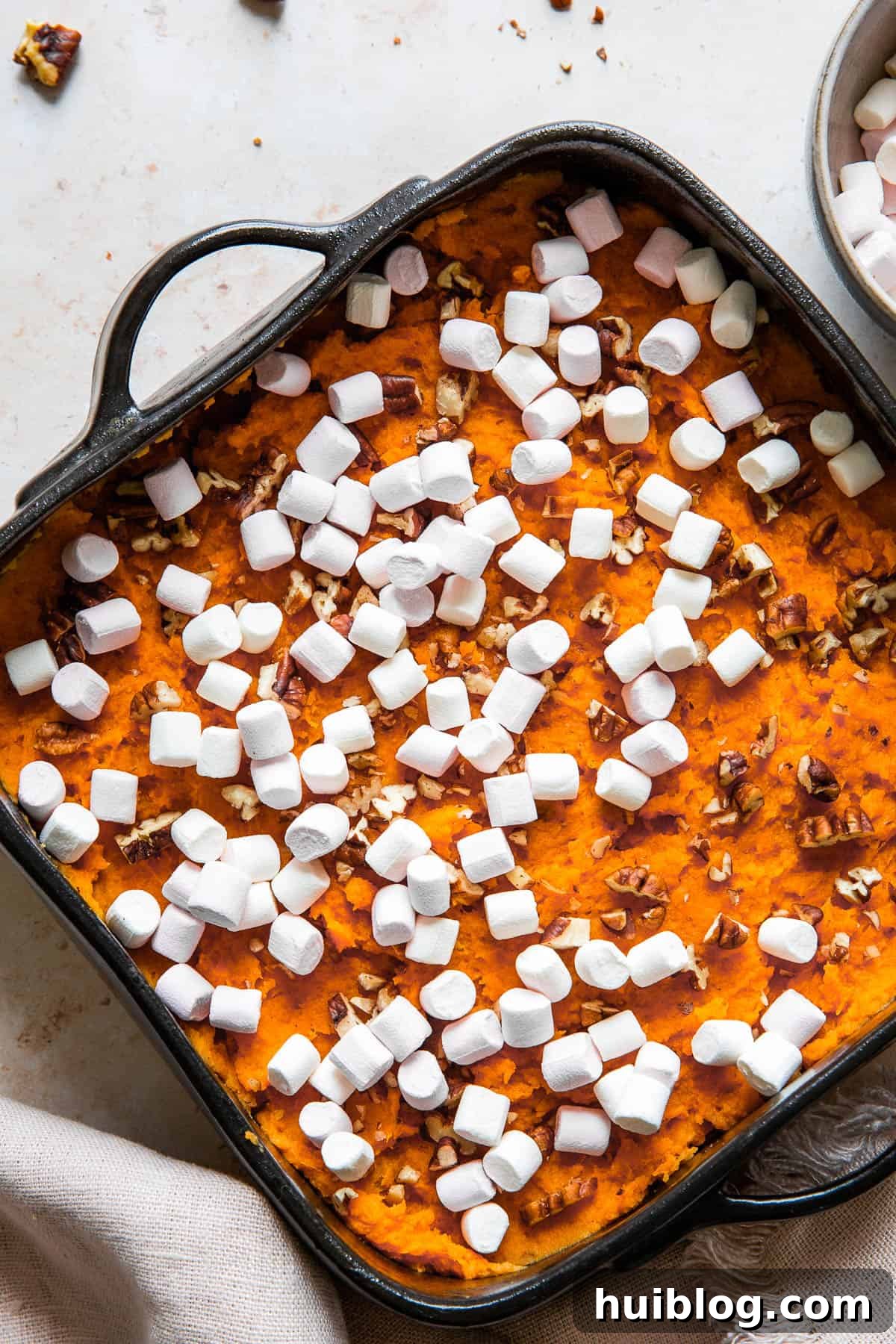 Close up shot of unbaked casserole, sprinkled with pecans and mini marshmallows.