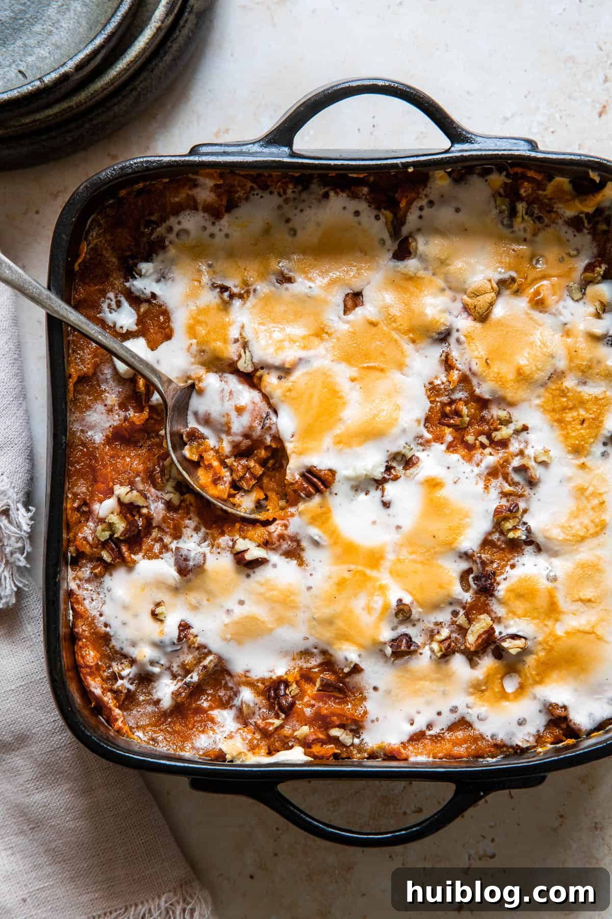 A serving spoon resting in a square black baking dish of sweet potato casserole.