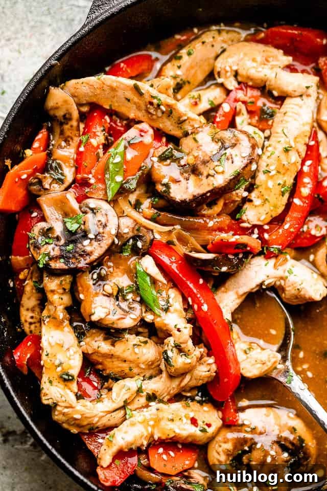 Skillet with chicken stir fry garnished with green onions and sesame seeds