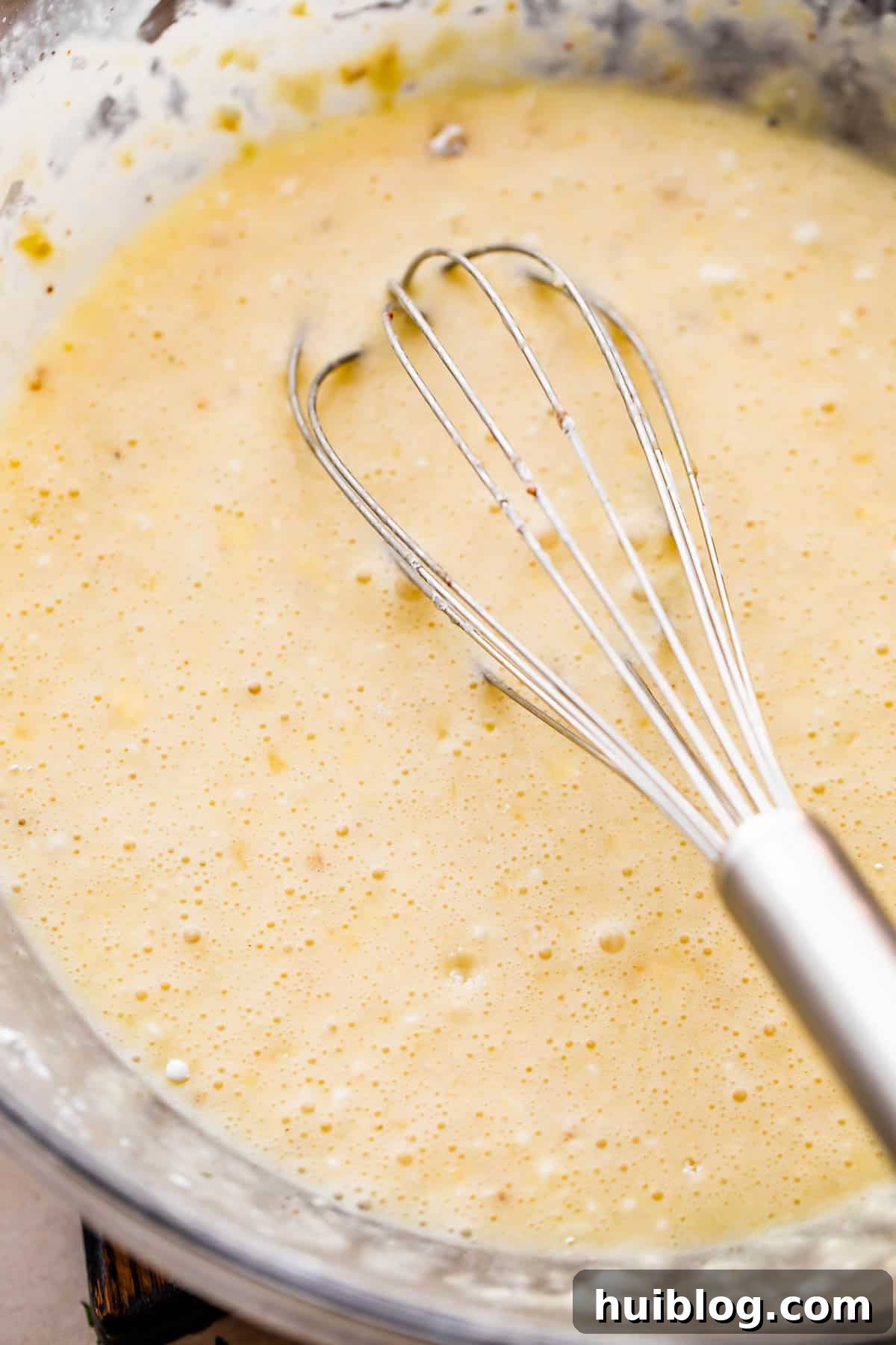 Melted butter, sugar, cornstarch, and cream being whisked together in a clear glass mixing bowl, forming the base of the custard.