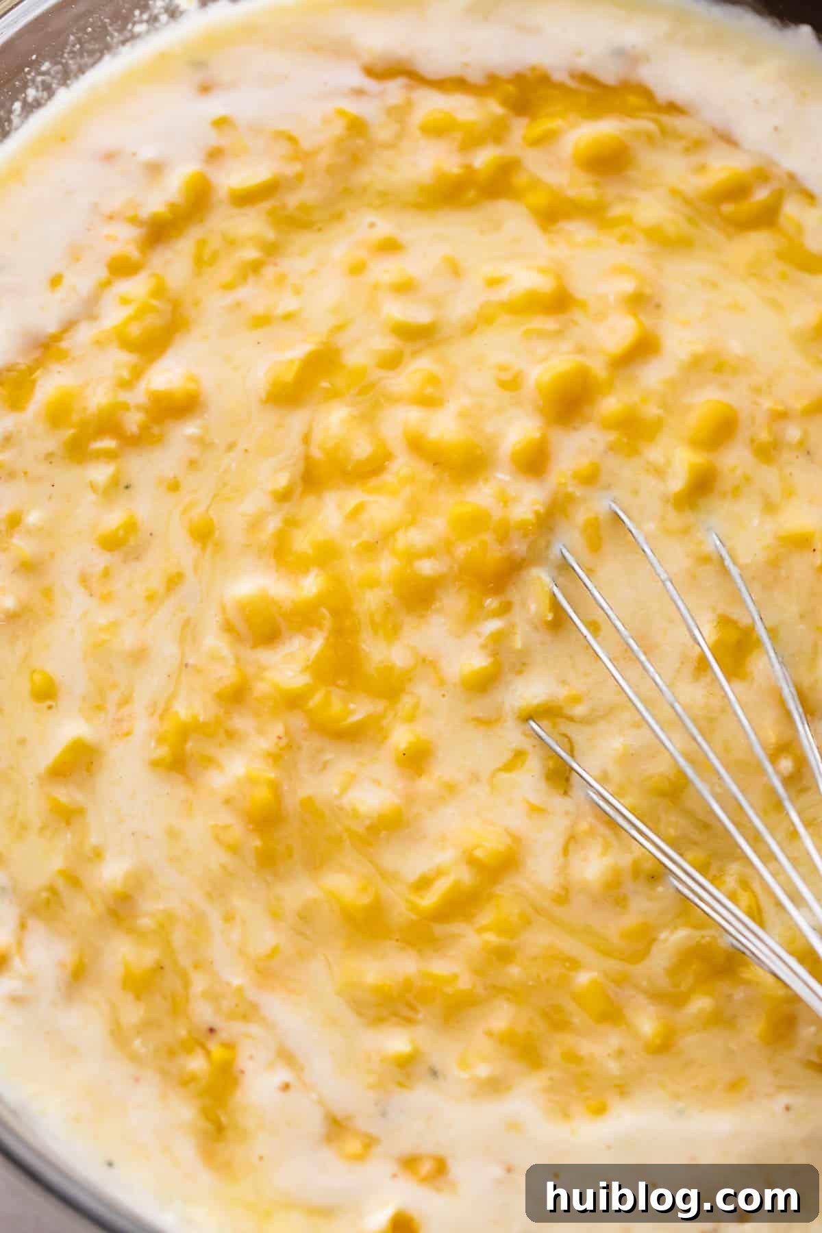 A glass mixing bowl filled with the creamy, yellowish corn pudding batter, before baking.