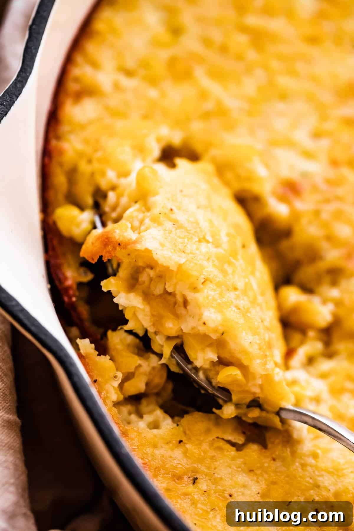 A close-up shot of the baked creamed corn casserole in a white skillet, with a serving spoon resting in it, ready to be dished out.