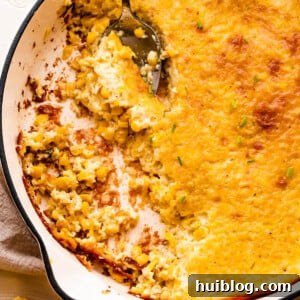 A spoon lifting a serving of creamed corn pudding from a white cast iron skillet.