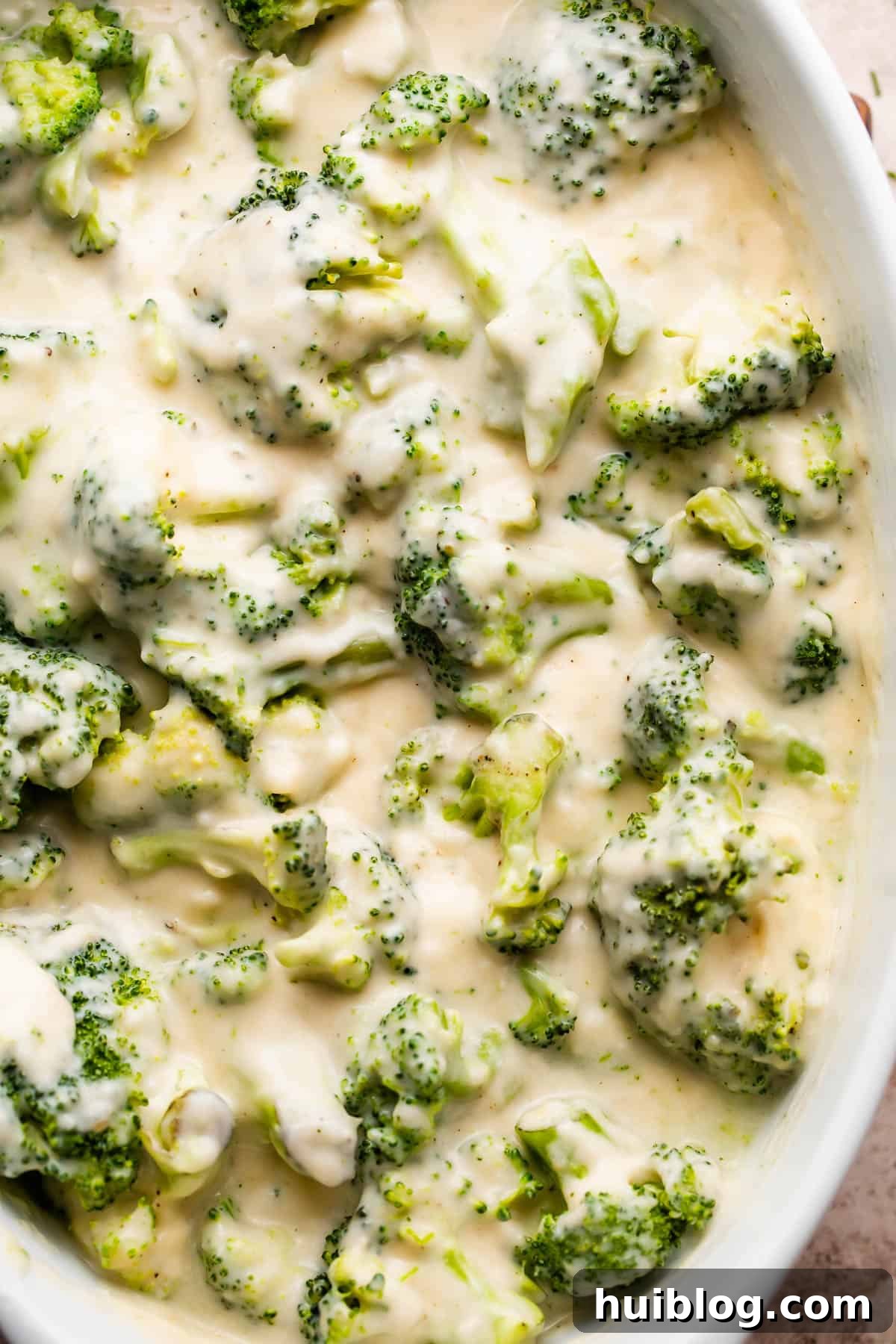 Close-up of vibrant green broccoli florets generously coated in a rich, creamy cheese sauce, ready for baking.