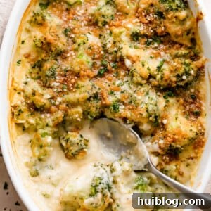 Overhead shot of an oval baking dish with Creamy, Cheesy Broccoli Casserole and a spoon mixing through it.