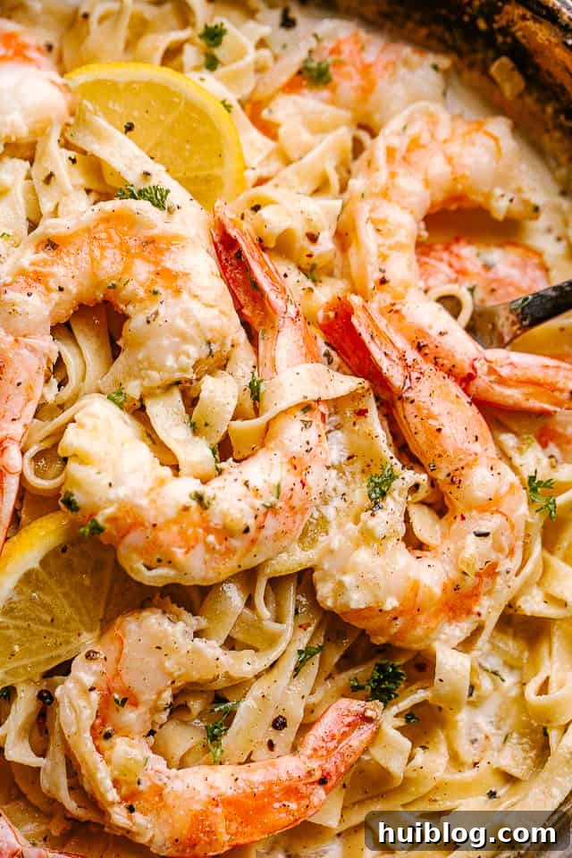 Creamy shrimp Alfredo pasta with my easy homemade Alfredo sauce! Made in only one pot, this pasta dinner idea is ready in under 30 minutes! Close up of Creamy Shrimp Alfredo Pasta in a pan garnished with lemon wedges.
