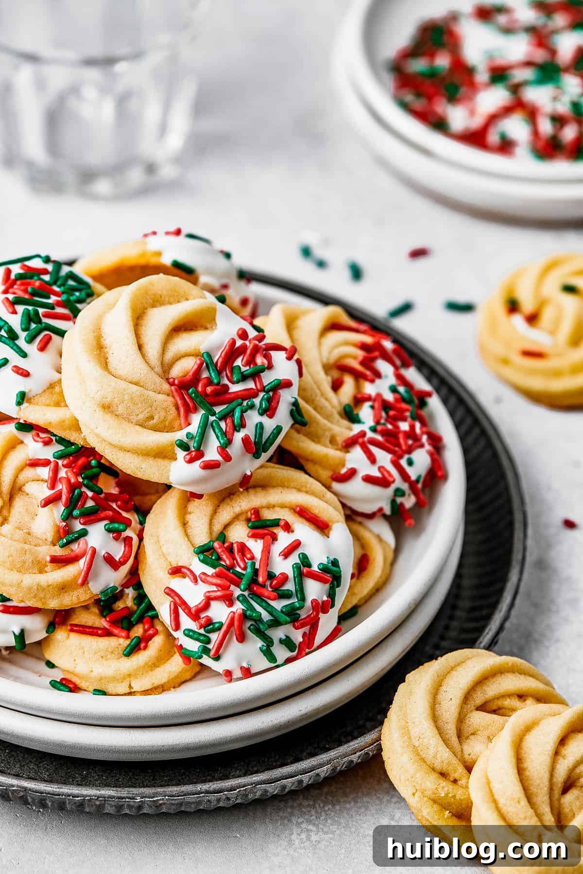 A small dessert plate artfully stacked on top of several other plates, brimming with beautifully iced butter cookies, creating an inviting and abundant display.