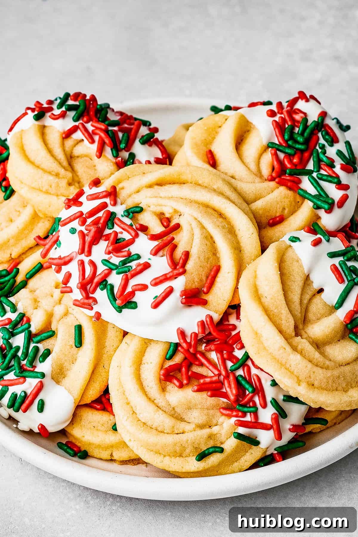 Butter cookies beautifully decorated with a delicate white chocolate drizzle and vibrant red and green sprinkles, perfect for holiday celebrations.