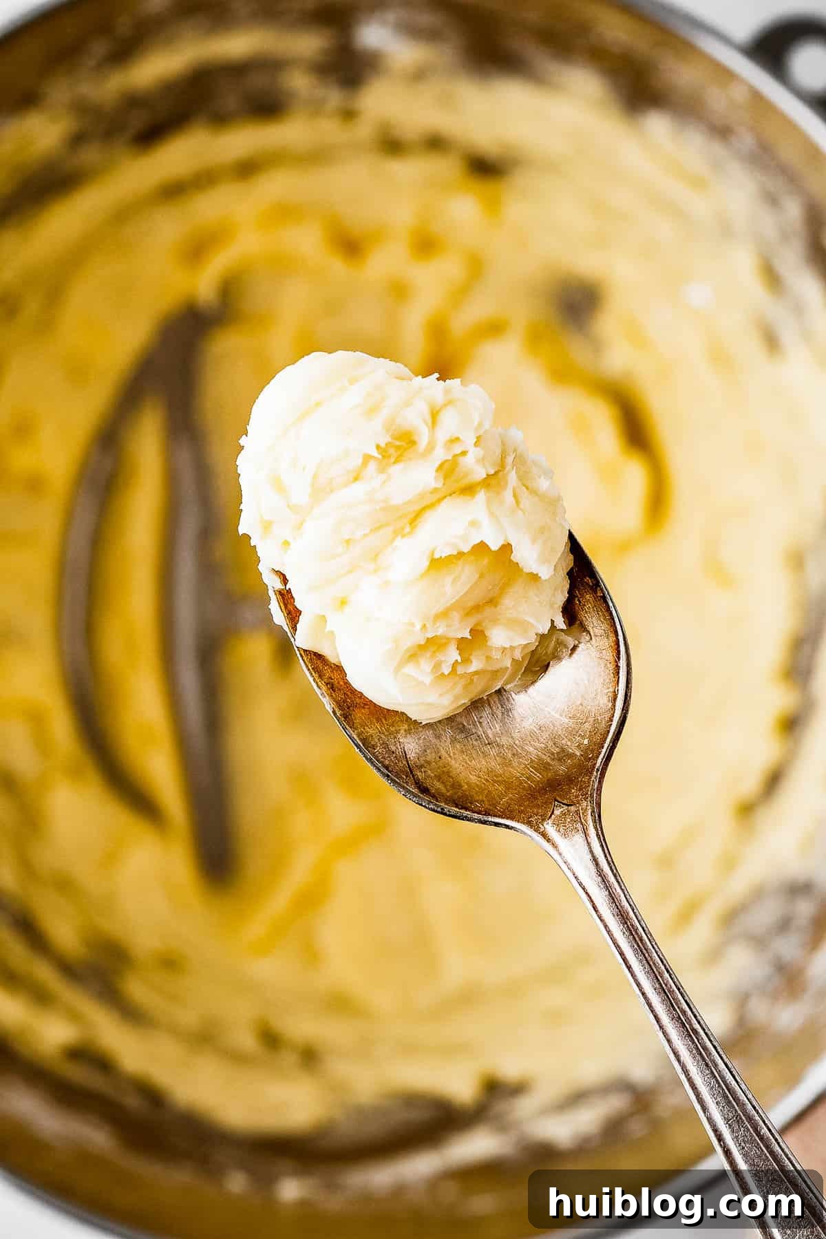 A spoon delicately lifting a small amount of soft, pliable cookie dough from a mixing bowl, showcasing its smooth consistency.