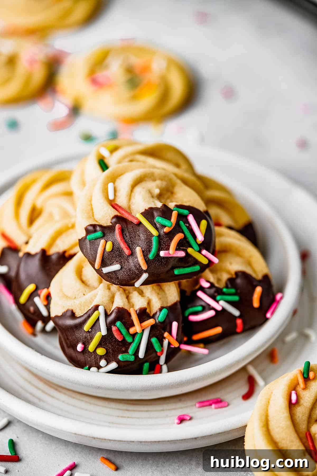 Close-up shot of decadent chocolate-iced butter cookies adorned with vibrant multicolor sprinkles, elegantly arranged on a crisp white plate, ready to be enjoyed.