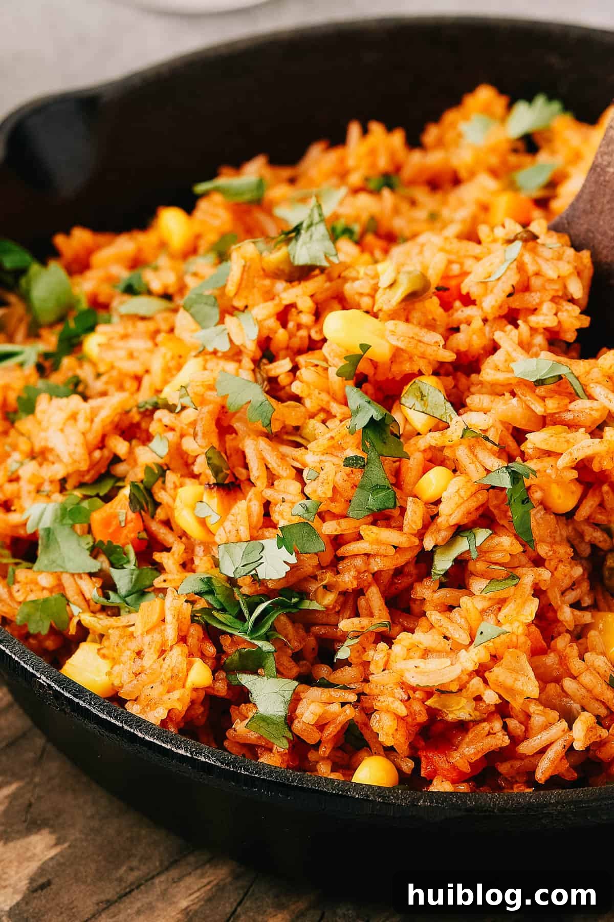 Side view of vibrant Instant Pot Mexican Rice in a cast iron skillet, with a wooden serving utensil.