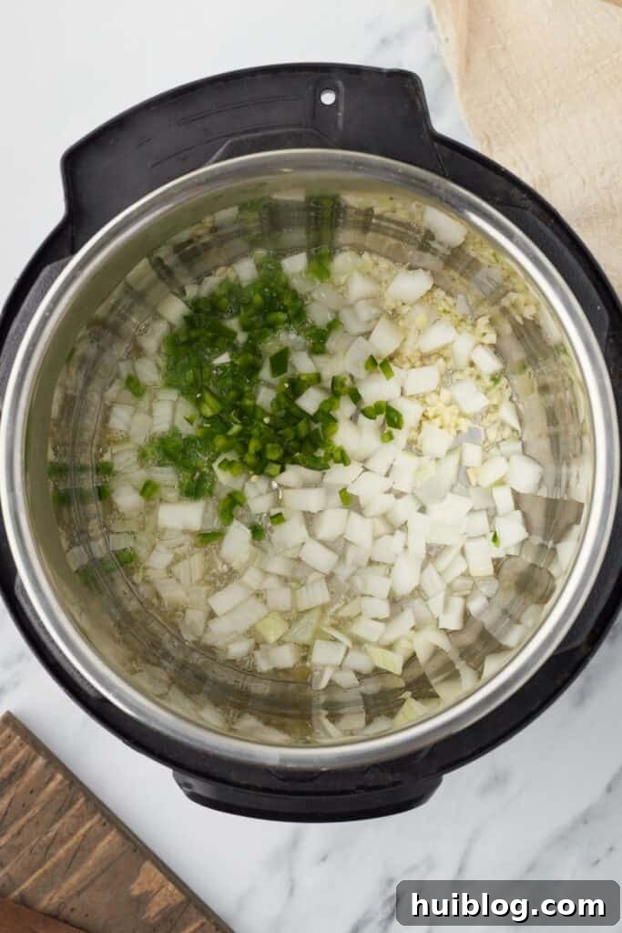 Overhead shot of an Instant Pot with chopped onions, garlic, and jalapeño sautéing in oil.