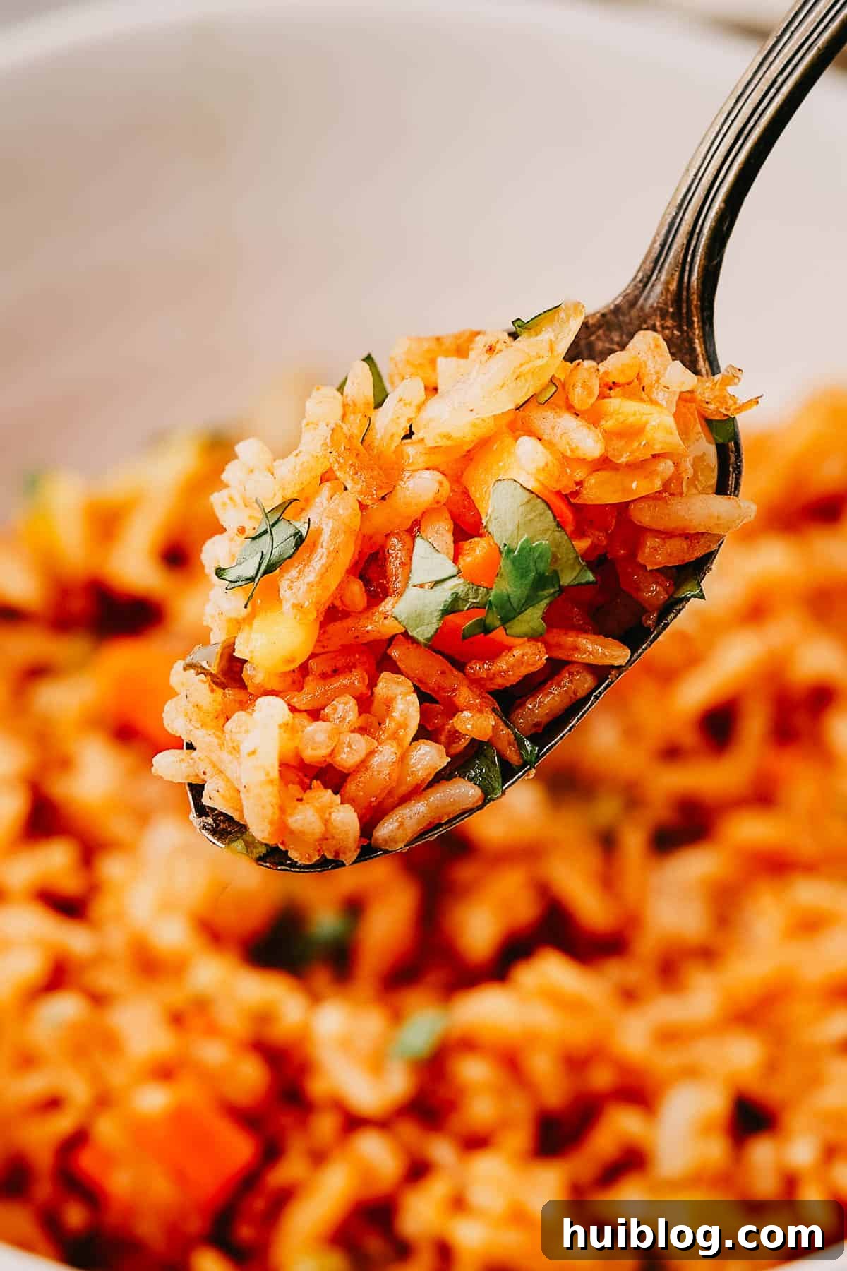 A spoon lifting a perfect bite of fluffy Instant Pot Mexican Rice out of a serving bowl, garnished with cilantro.
