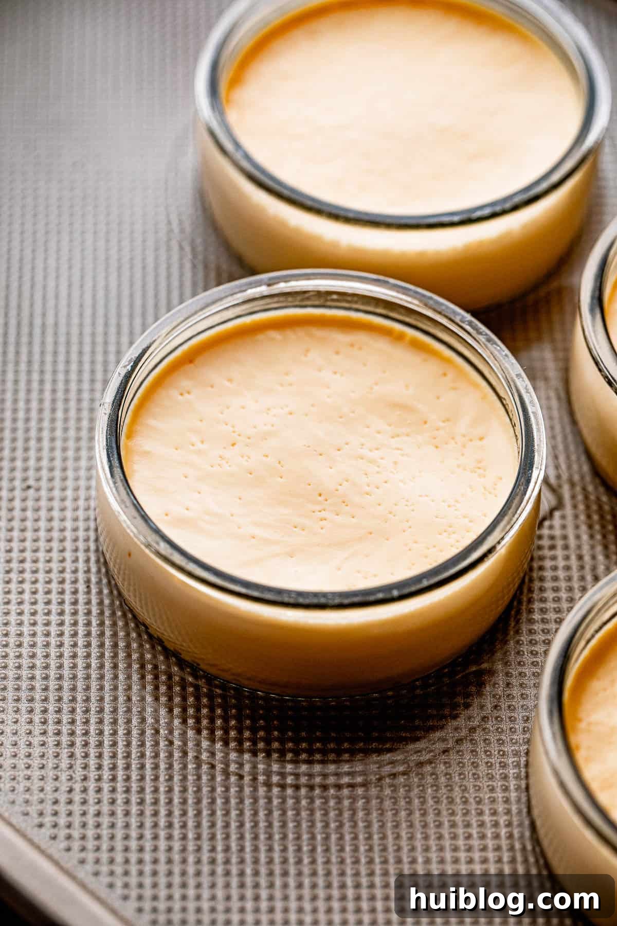 side shot of two jars with creme brulee set on a sheet pan with water.