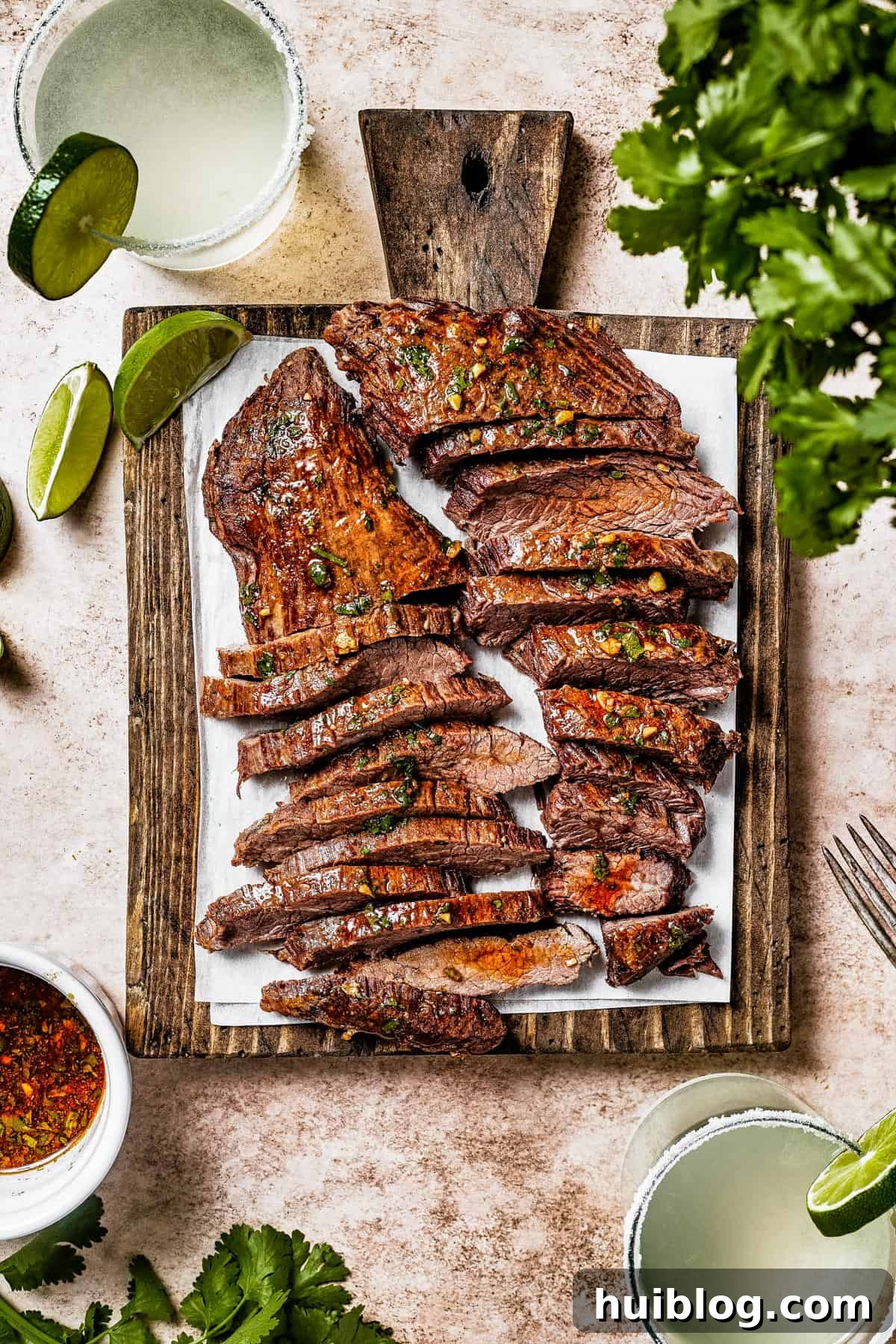 A cutting board with thinly sliced steak, garnished with lime wedges and fresh cilantro.
