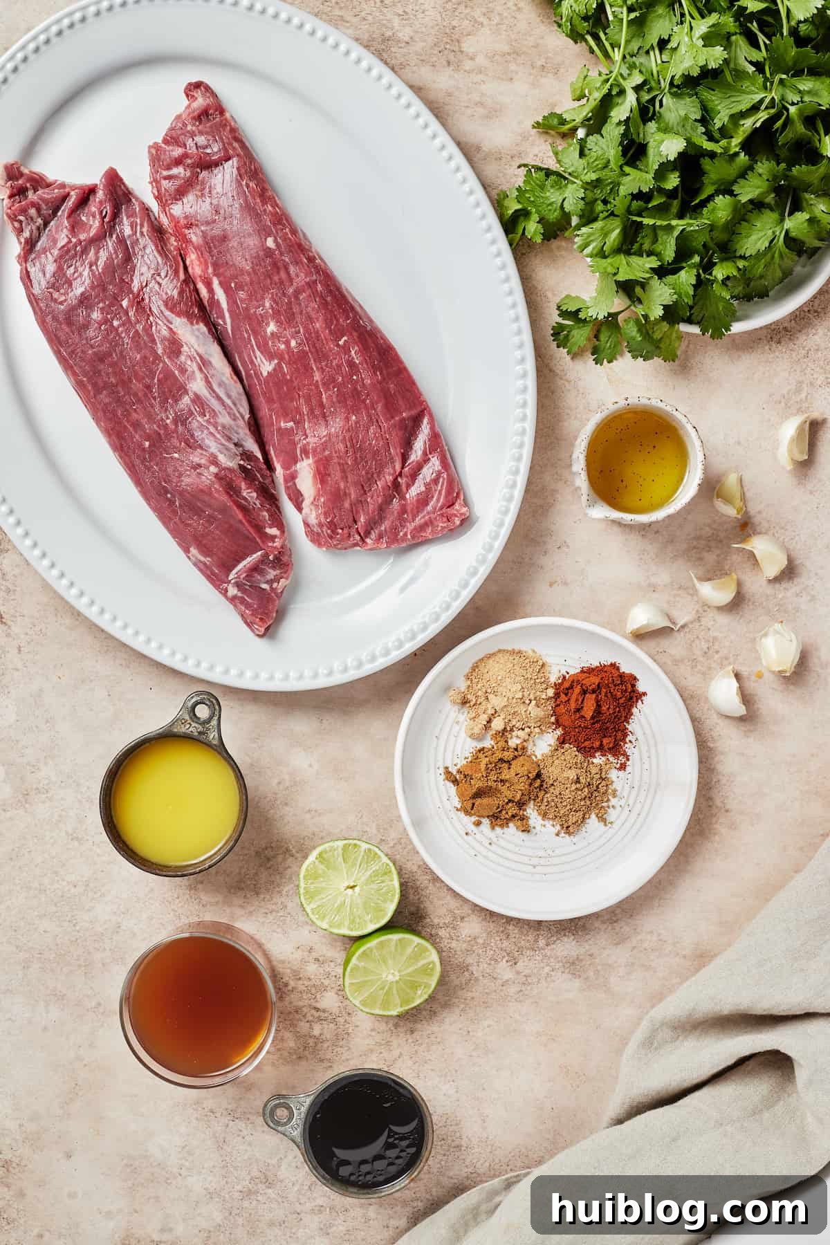 Various ingredients for Instant Pot Carne Asada including flank steak, cilantro, avocado oil, garlic, spices, limes, tamari, beef broth, and orange juice.